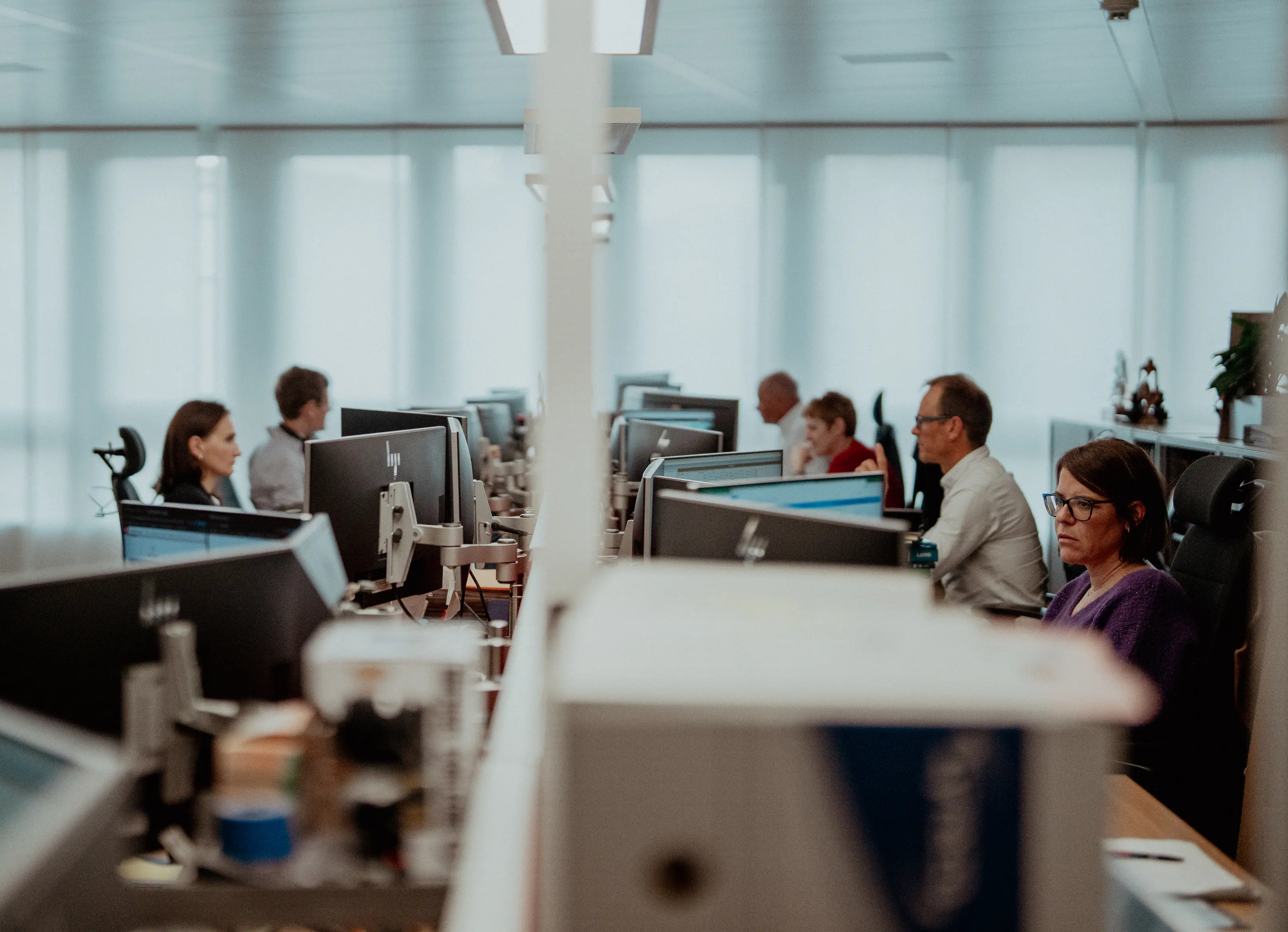 People working at computer desks in a modern office with large windows.
