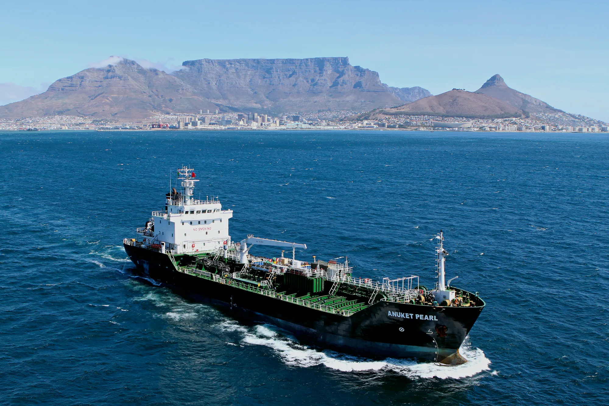 Cargo ship sailing near Table Mountain with a city skyline in the background.