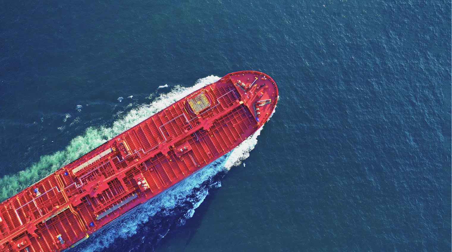 Red cargo ship sailing through deep blue ocean, top-down aerial view.