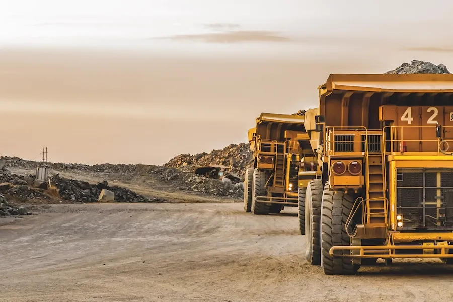 Large yellow mining trucks driving on a dirt road at a quarry.