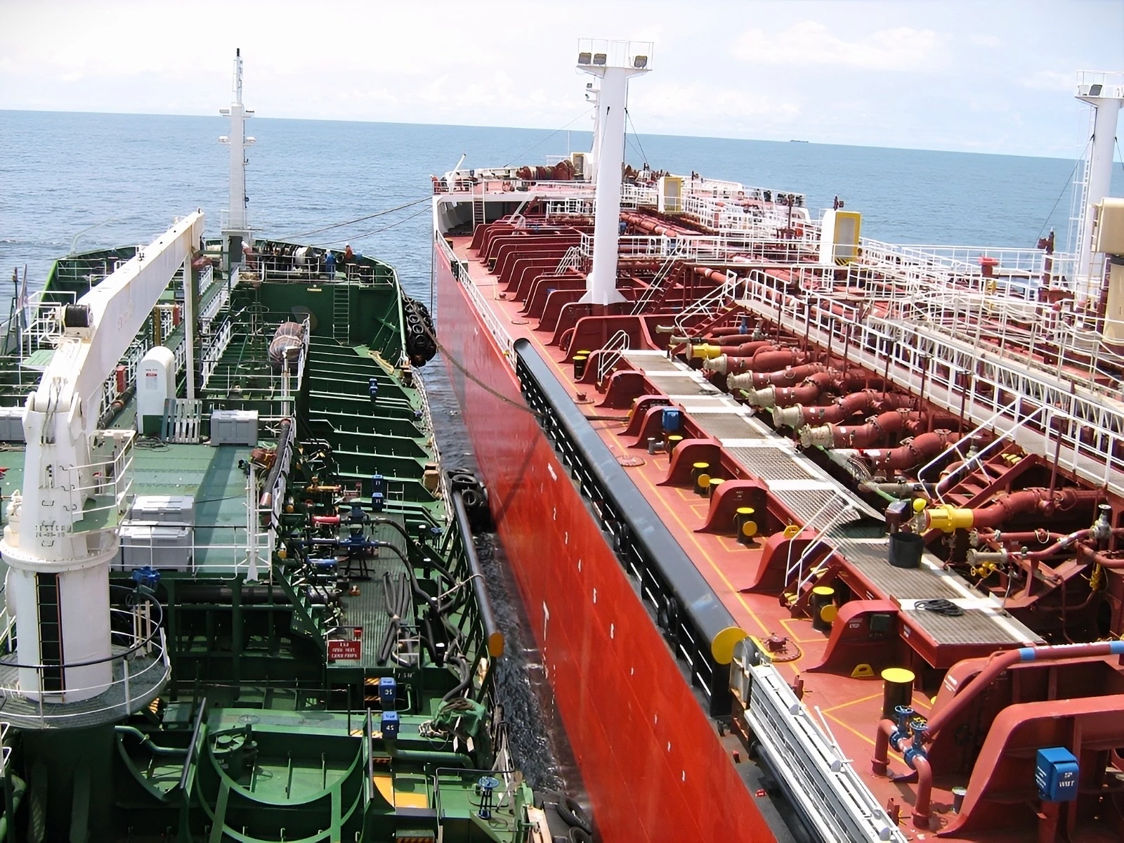 Two large tankers at sea, connected side by side for cargo transfer.